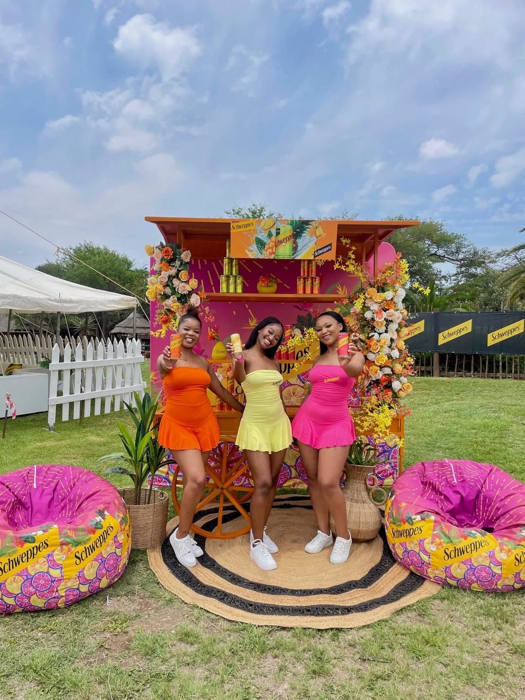 Brand ambassadors in orange, yellow and pink in front of a floral Schweppes cart