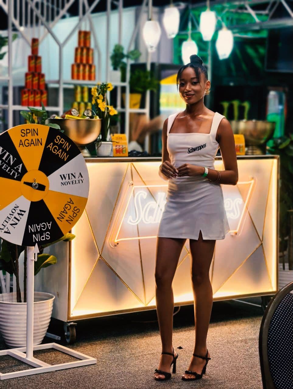 Brand ambassador in a Schweppes dress at a lit branded bar with a prize wheel