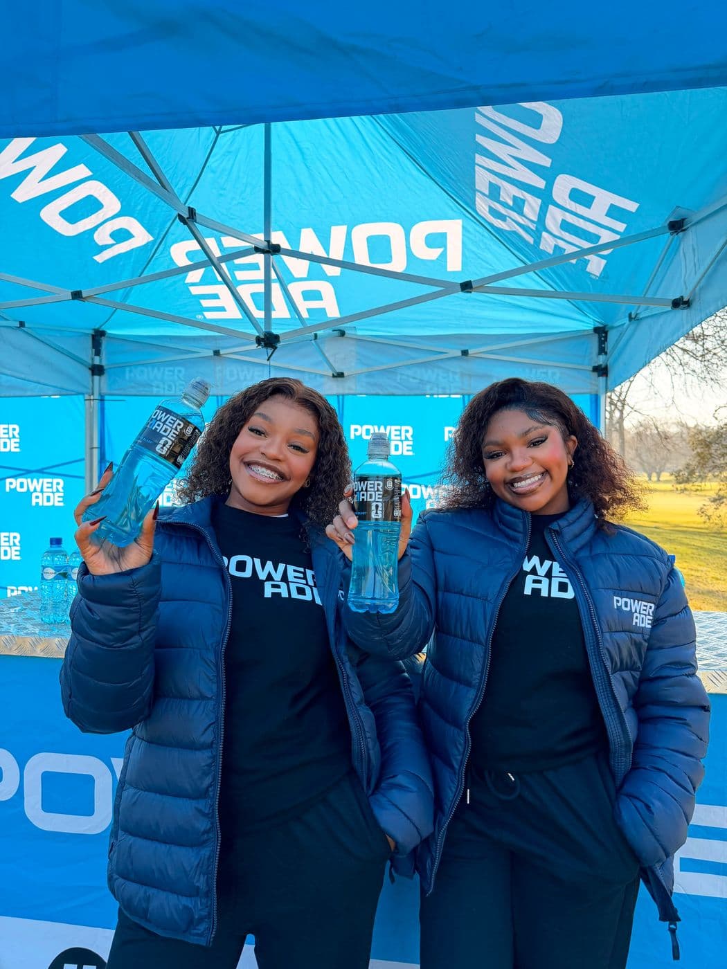 Two brand ambassadors in Powerade jackets holding bottles under a branded gazebo