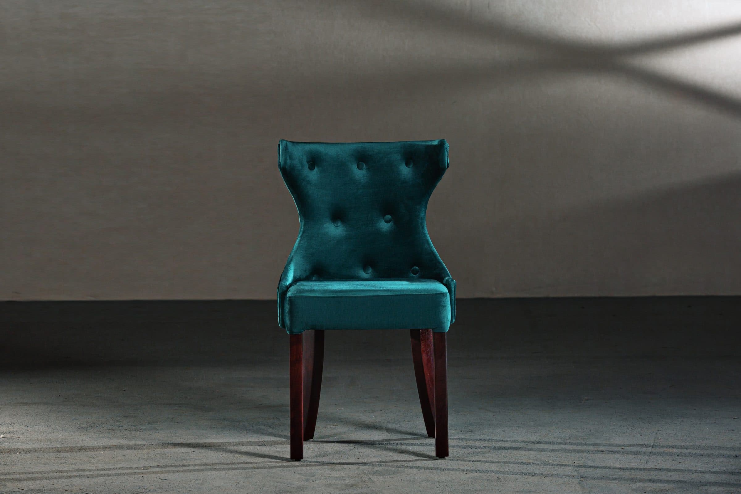 Deep teal buttoned velvet dining chair on a grey backdrop
