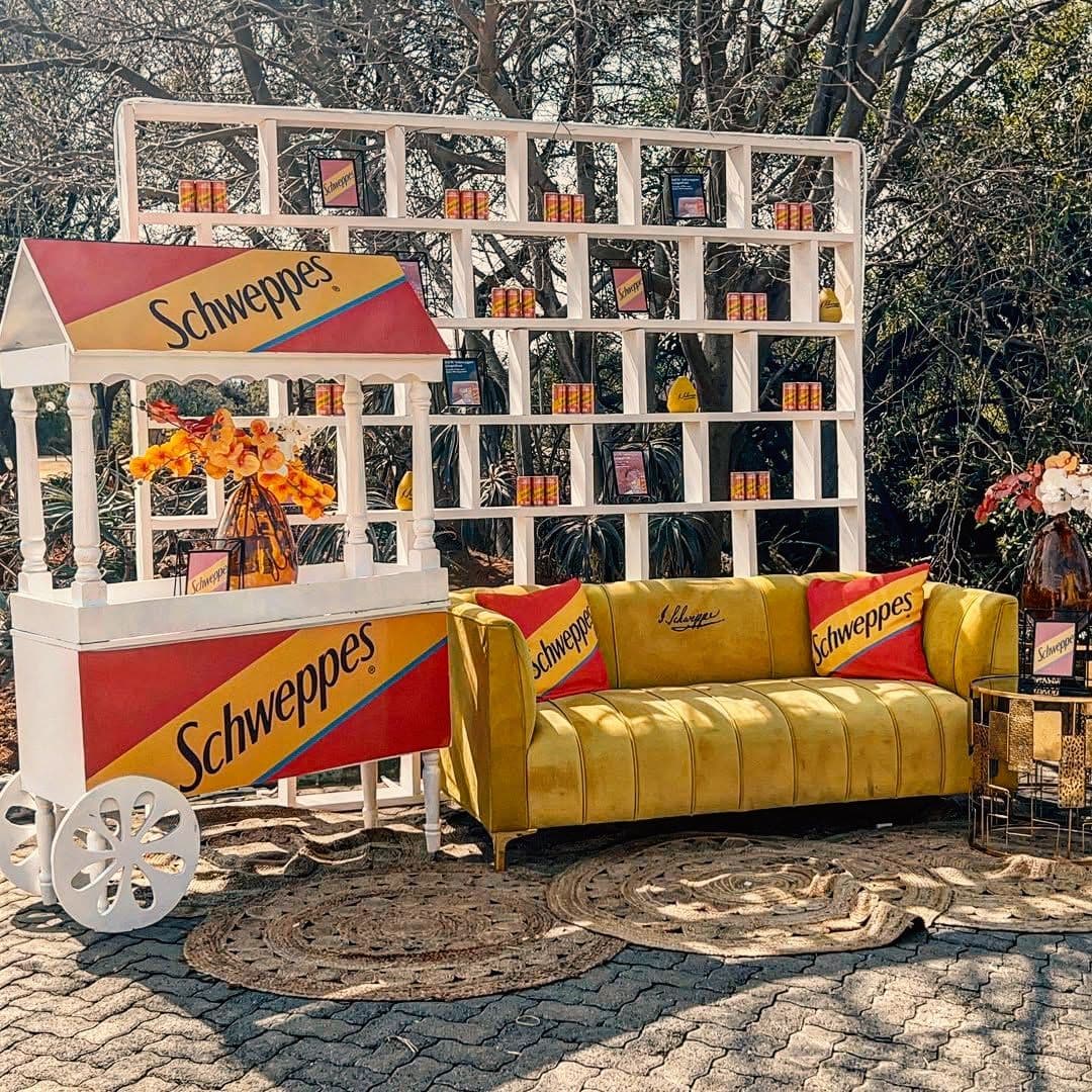 Schweppes lounge with a mustard velvet sofa, branded cushions and a white display shelf